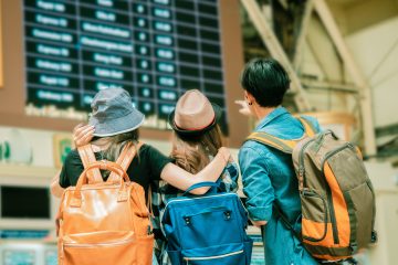 Friends wearing backpacks looking at time board to travel.