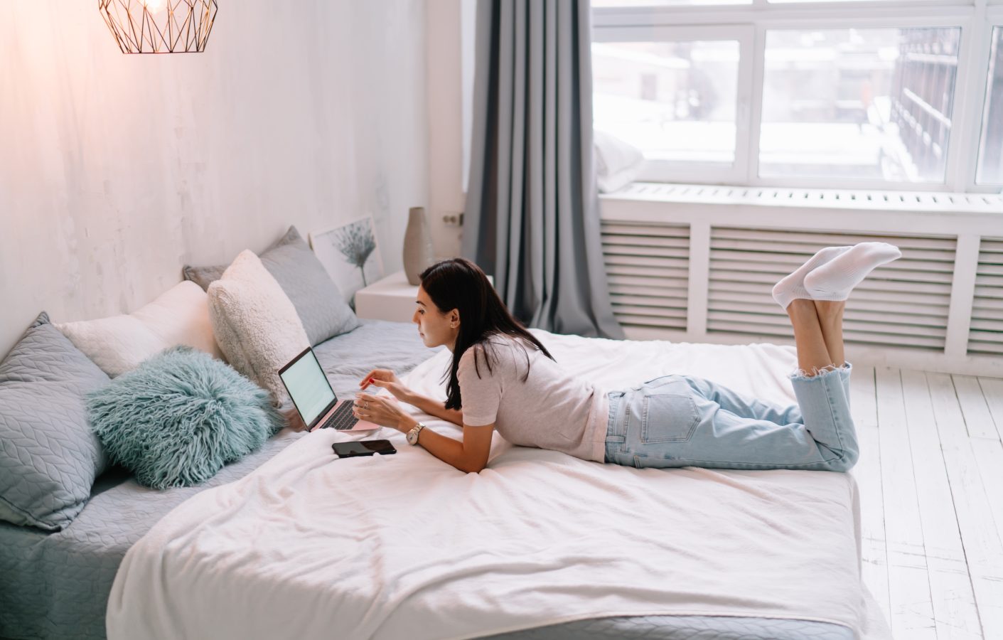 Side view of young asian woman using laptop while lying and resting on bed at home.