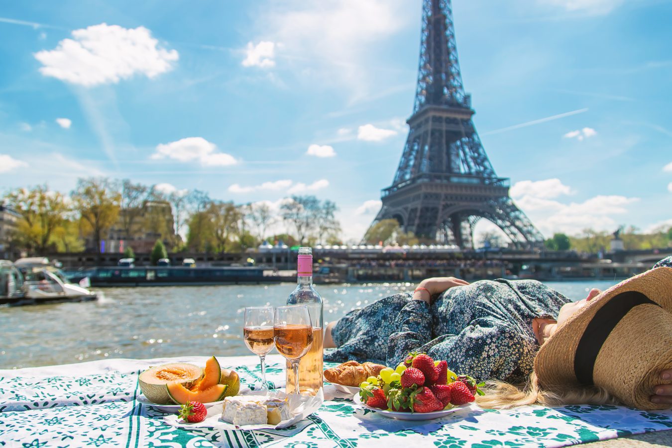 A woman lays on a blanket with a picnic spread next to here along the river in front of the
Eiffel Tower in Paris.