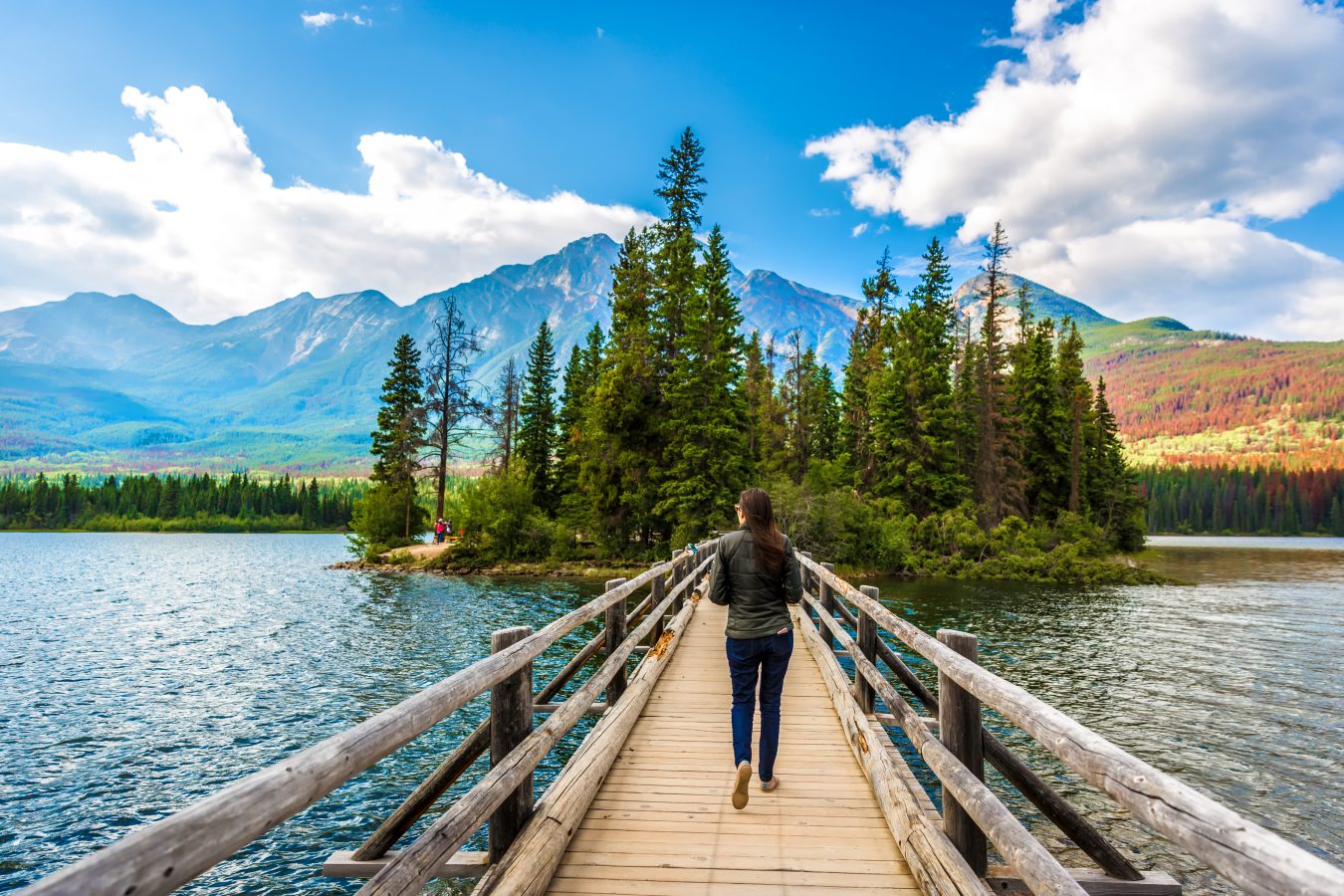 Young woman walking in a narrow wood bridge in front of an amazing scenario in Jasper National Park in Canada