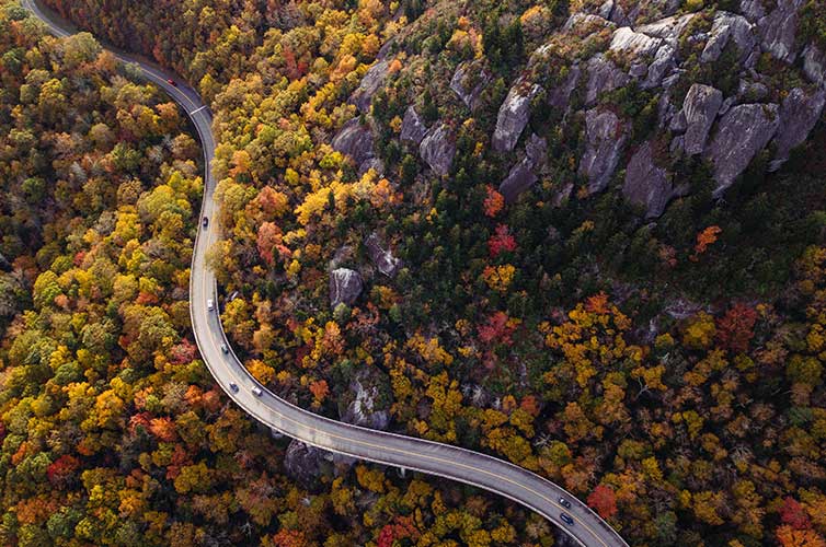 Winding road around mountain with trees showing fall foliage.