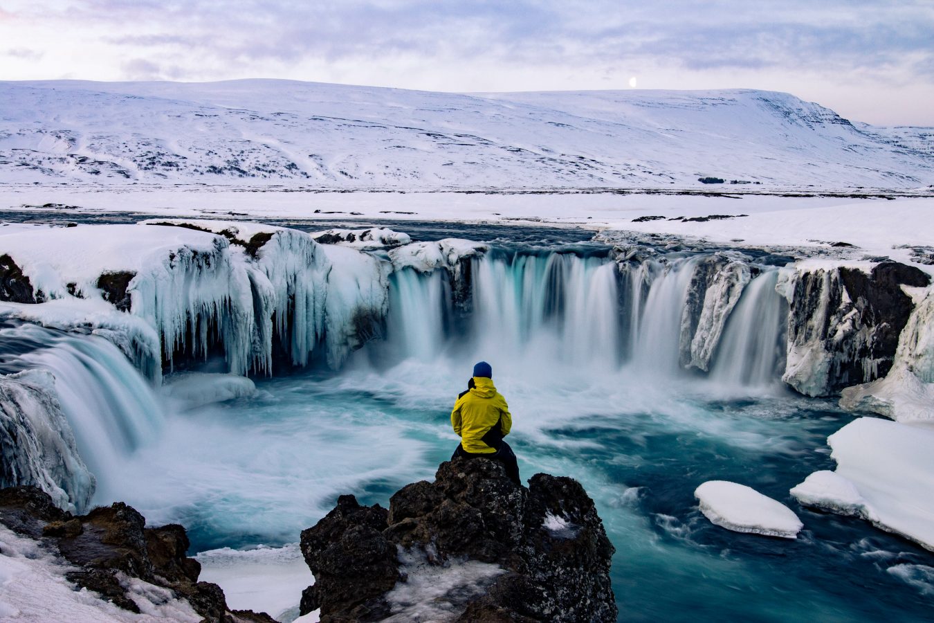 Traveler overlooking Godafoss, Iceland in winter. Flights to Iceland from the US can be super affordable!