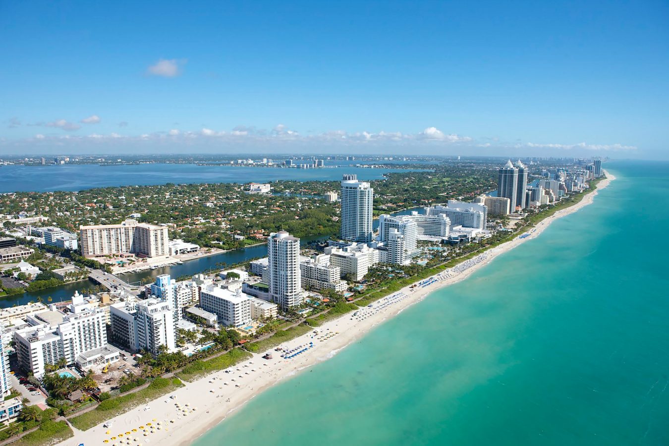 Aerial view of the Miami strip looking at the tall hotel buildings, the beach, and the light blue ocean. Miami is one of the cheapest destinations in 2024.