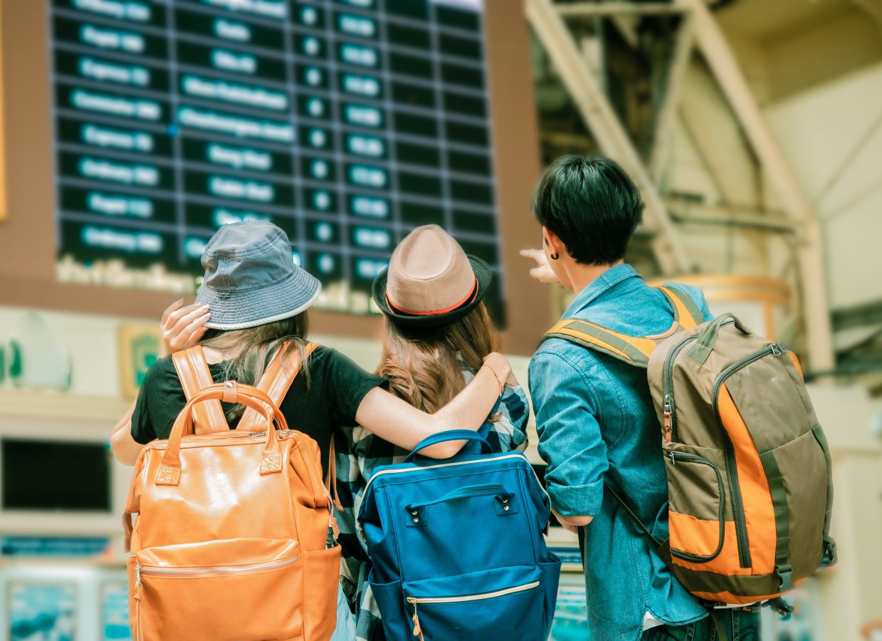 Friends wearing backpacks looking at time board to travel.