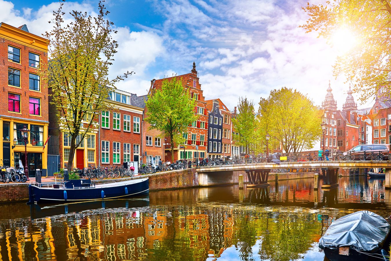 Channel in Amsterdam Netherlands with green summer season trees, houses, and bicycles.