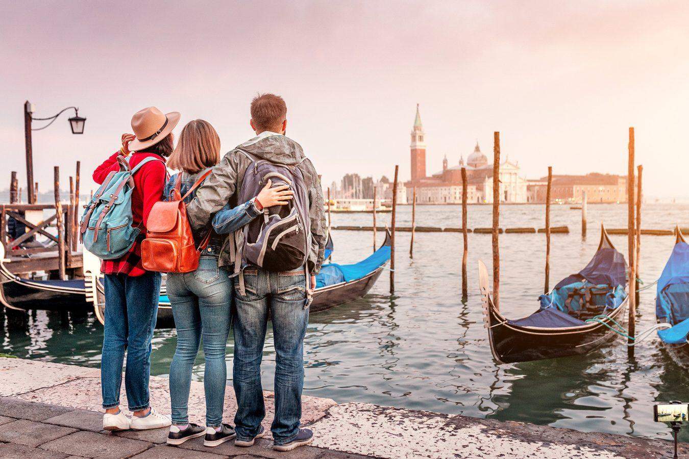 Group of study abroad friends having fun on San Marco Square with gondolas and Grand channel at the background in Venice.