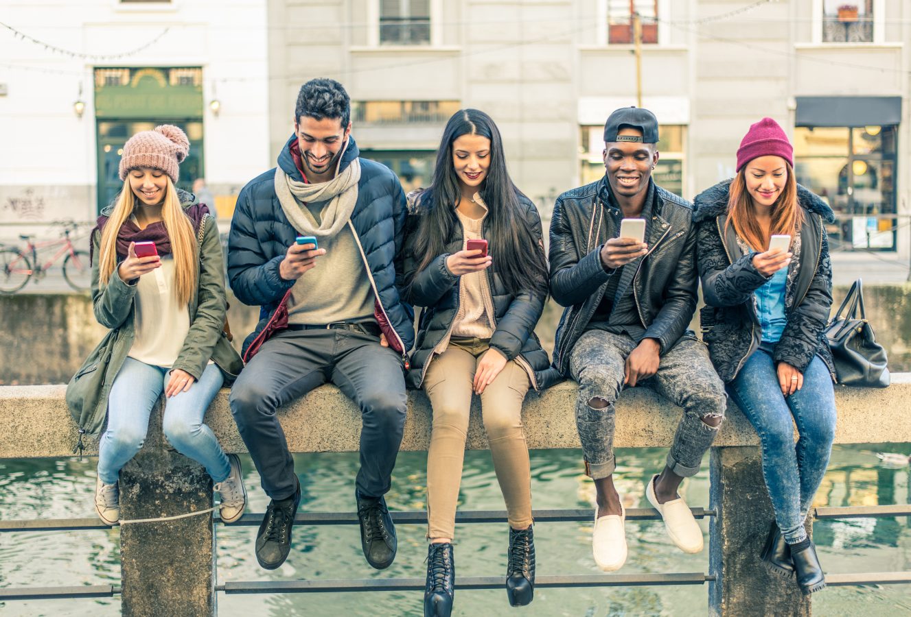 Multicultural group of students sitting together on their phones