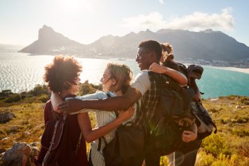 Group of four friends traveling together hug at the summit of their hike.