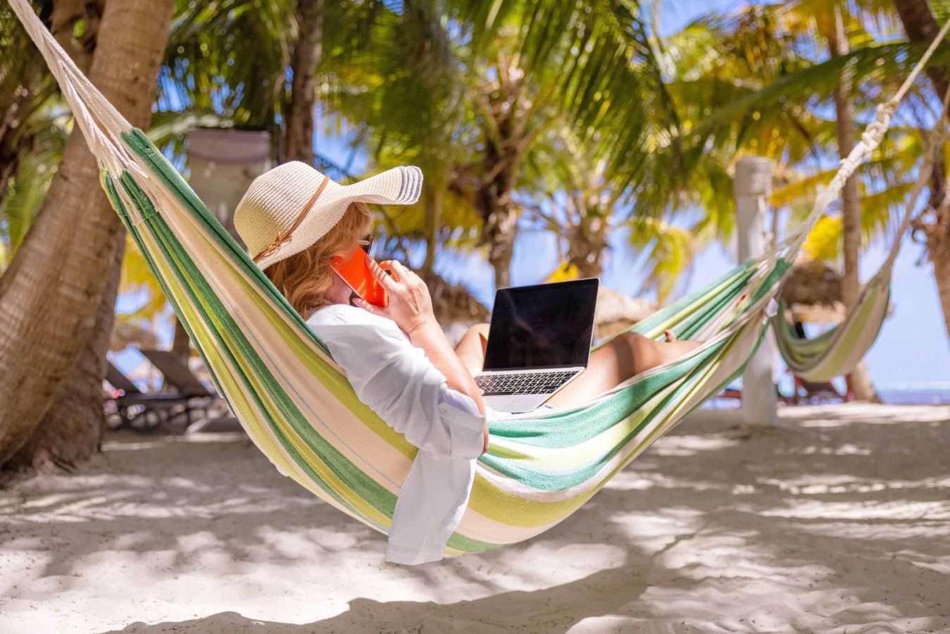 Woman lying in hammock on tropical beach and working on laptop a