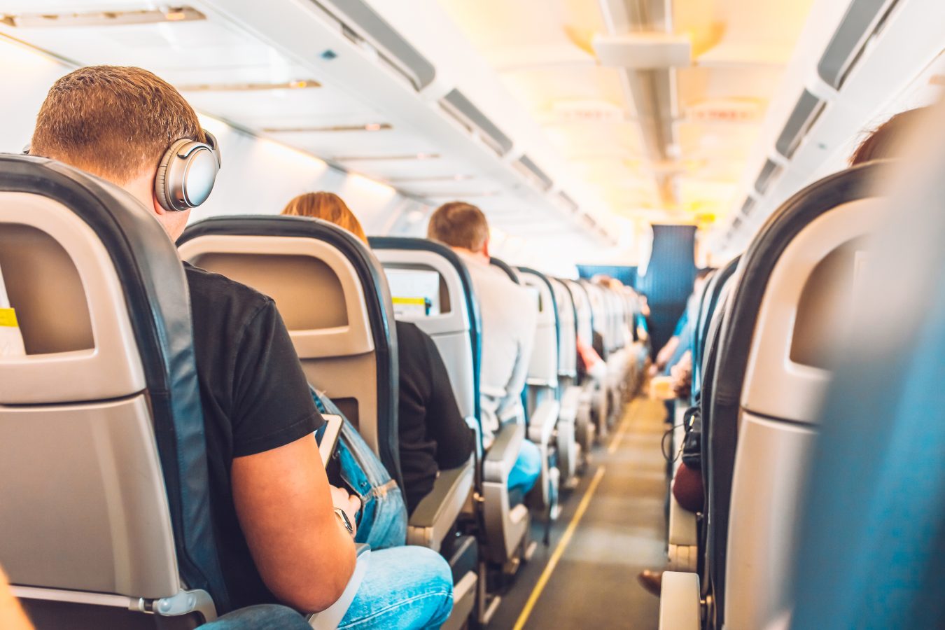 Airline passengers travel sitting on flight in economy class, some using devices with free wifi.