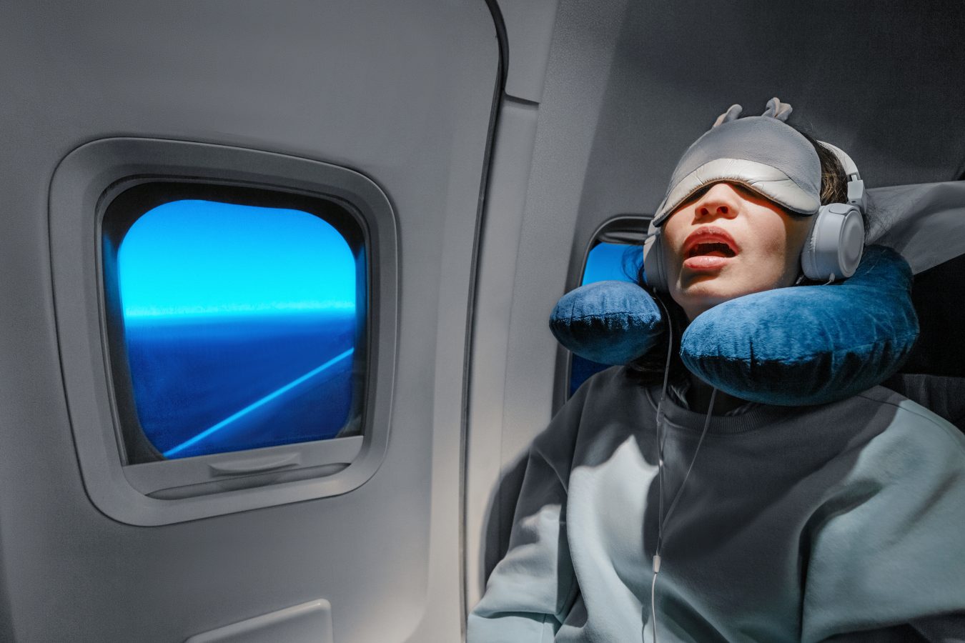 Asian girl sleeping in her seat on the plane near the window with her mouth open and in a mask and with a neck pillow to sleep, trying to avoid jetlag.