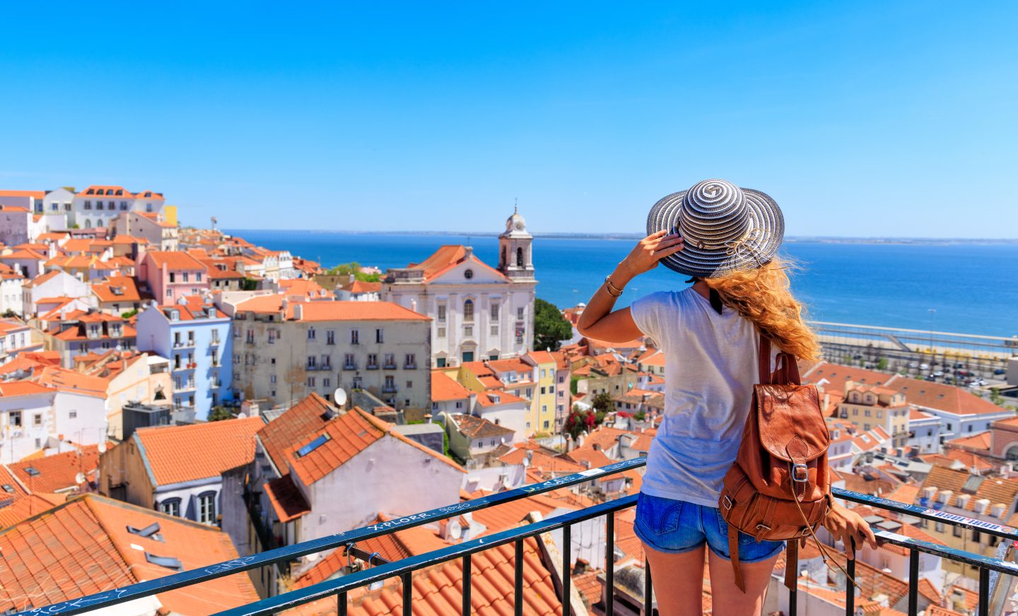 Traveler stands by railing overlooking the city of Lisbon, Portugal and the ocean beyond it.