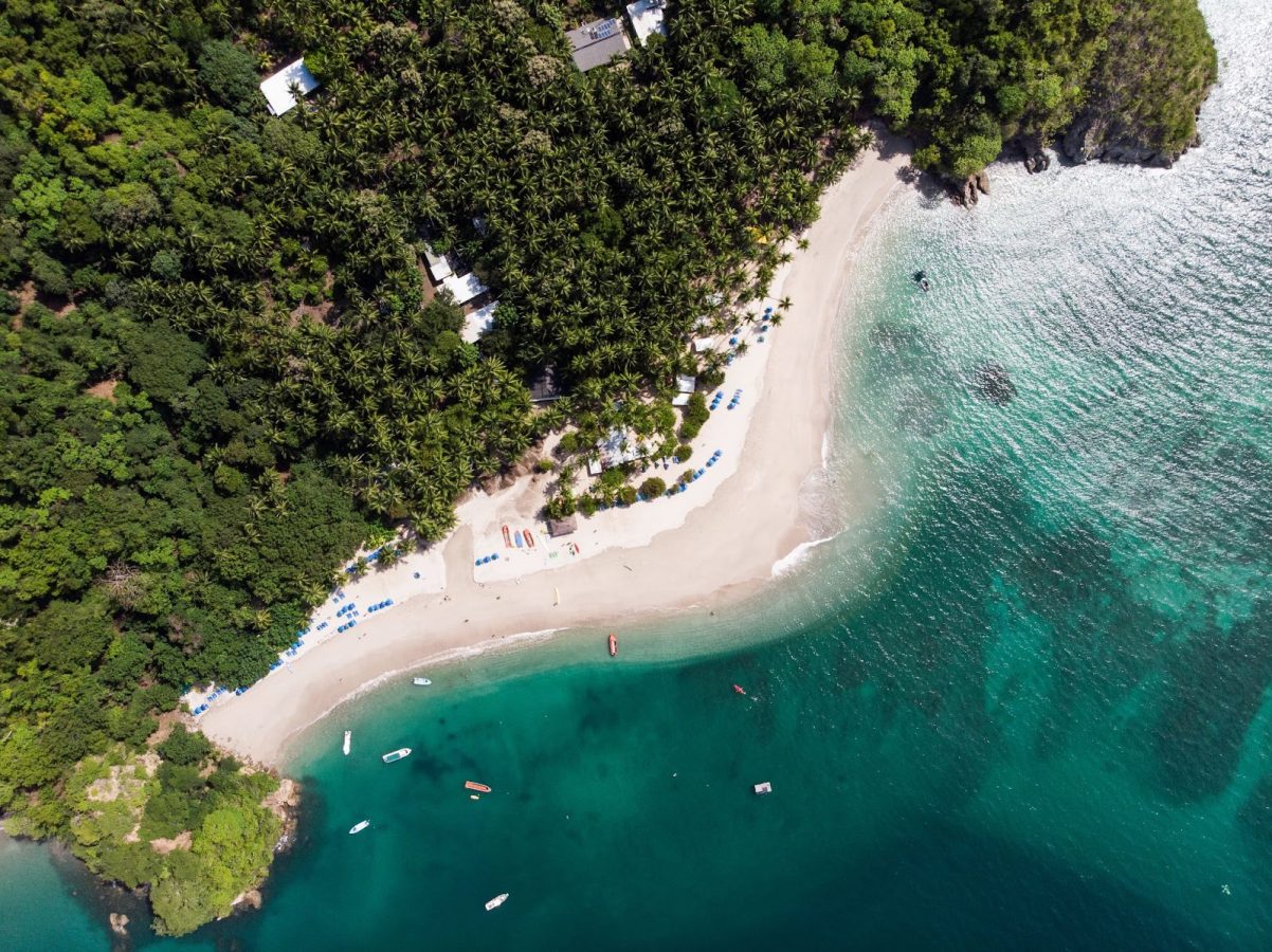 Aerial view of a beach in Costa Rica with green forest jungle above and deep blue-green waters below.