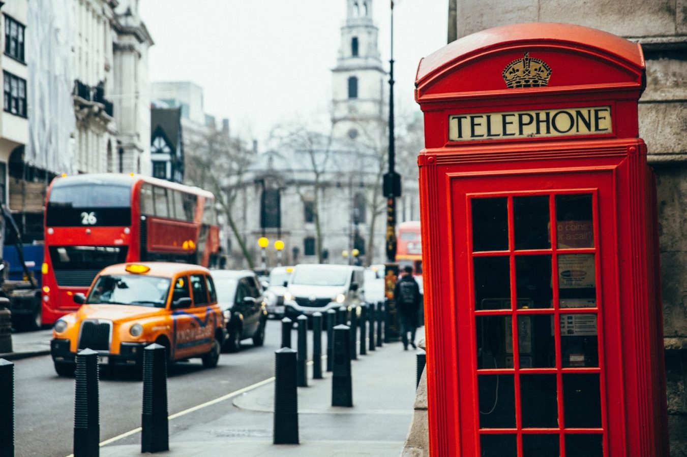 Busy street of London with a red telephone booth on the sidewalk.