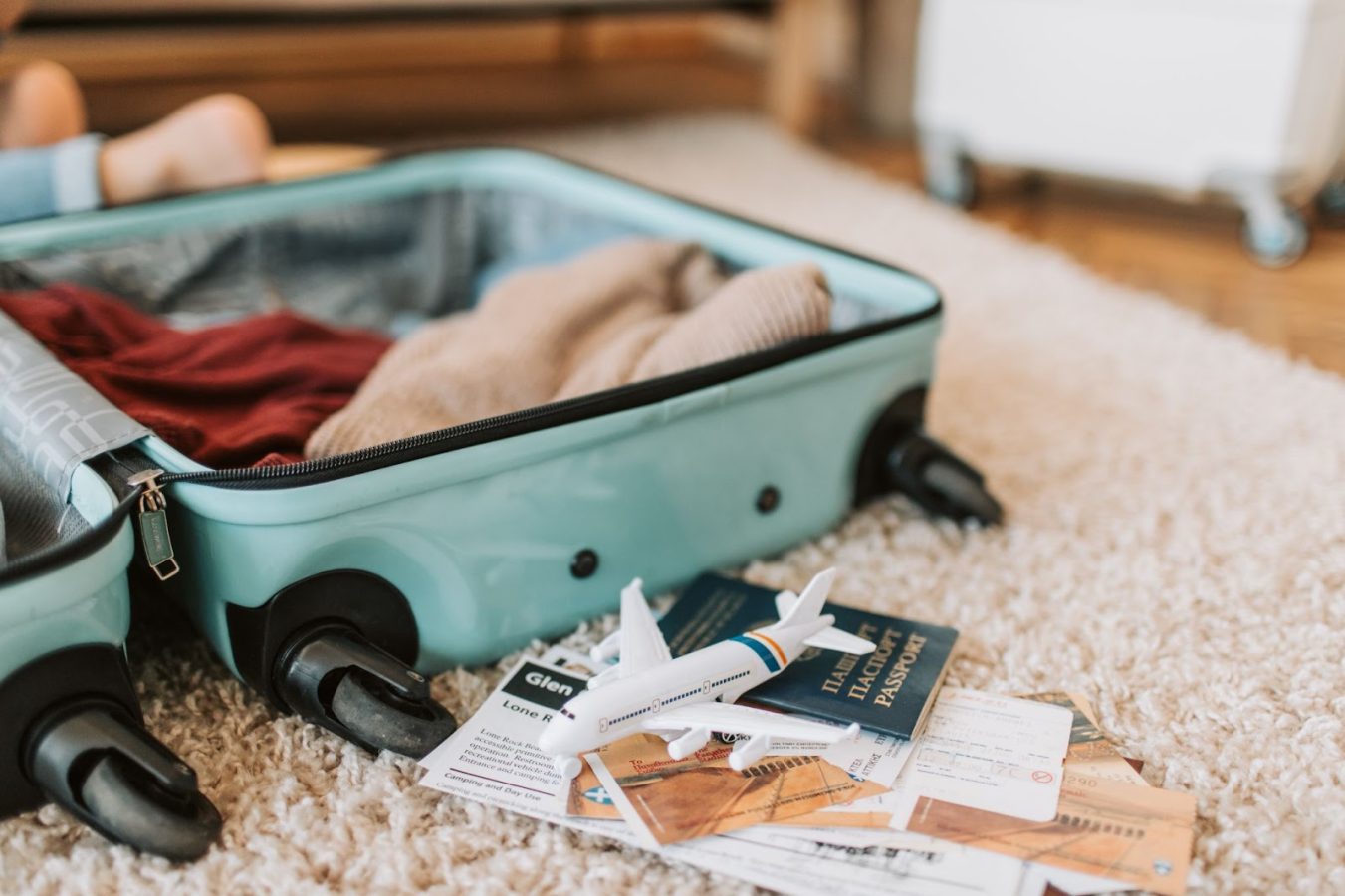 A partially packed suitcase with some clothes inside and papers, and passport on the floor beside it.