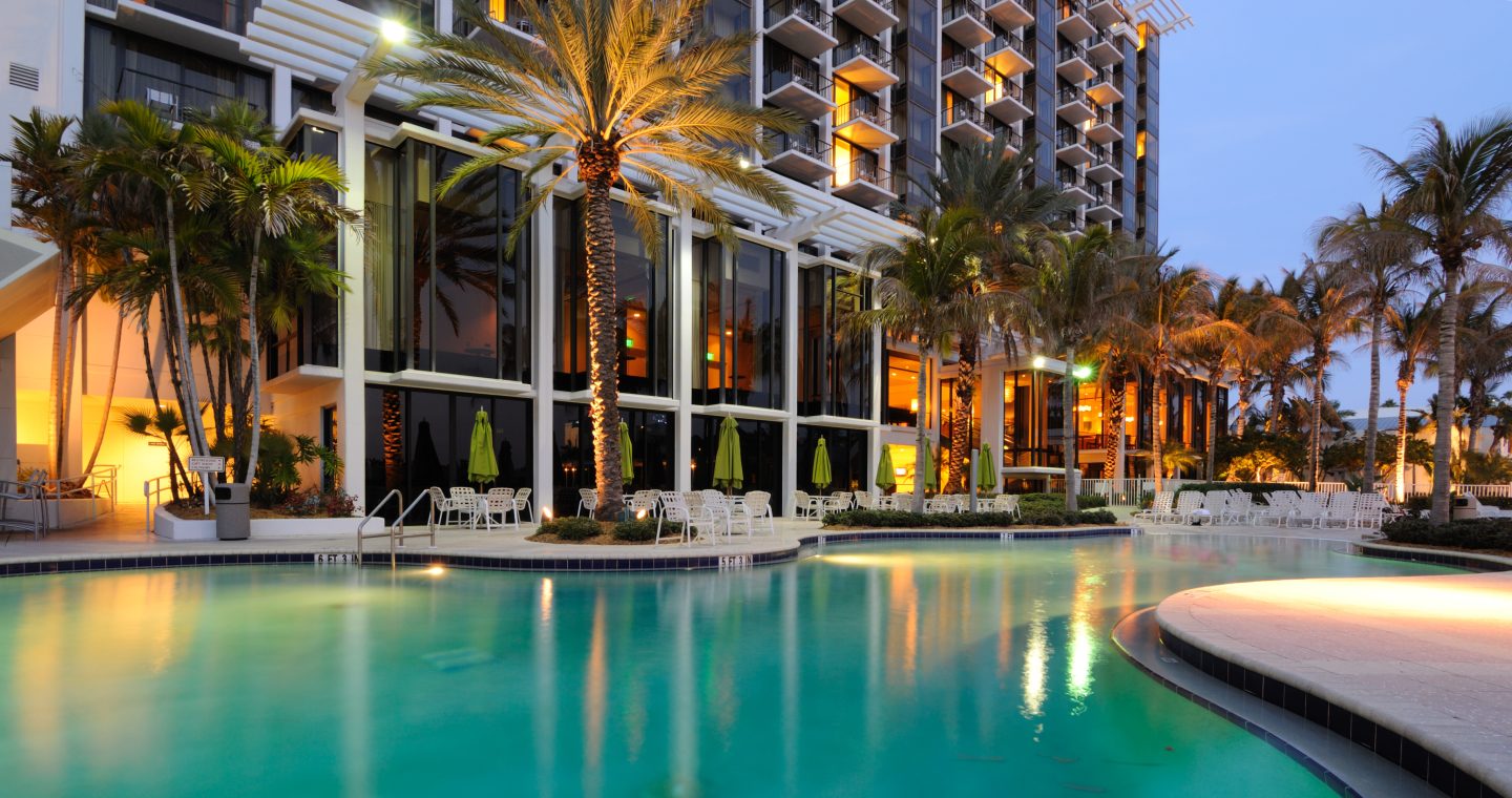 A swimming pool outside a hotel resort with a palm tree next to the pool in the evening.