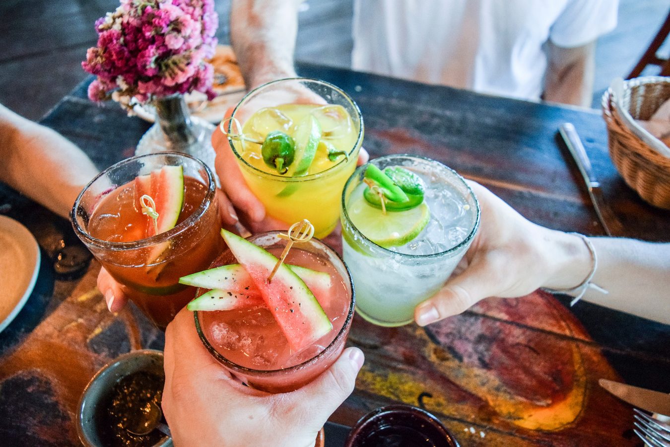 Group of four friends cheers their cocktails or mocktails at a dinner table.