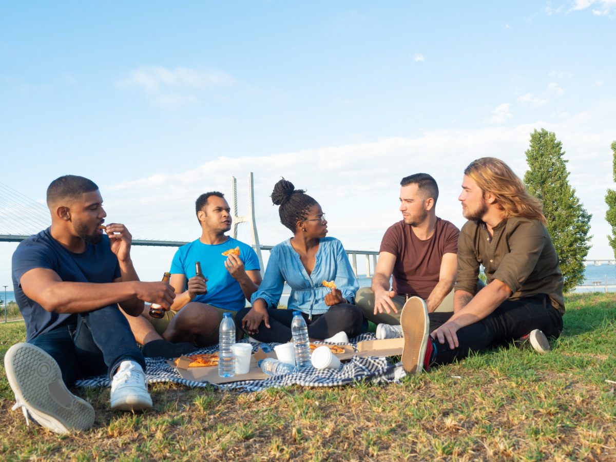 Group of new friends met during a cultural immersion experience sit in a park for a picnic together.