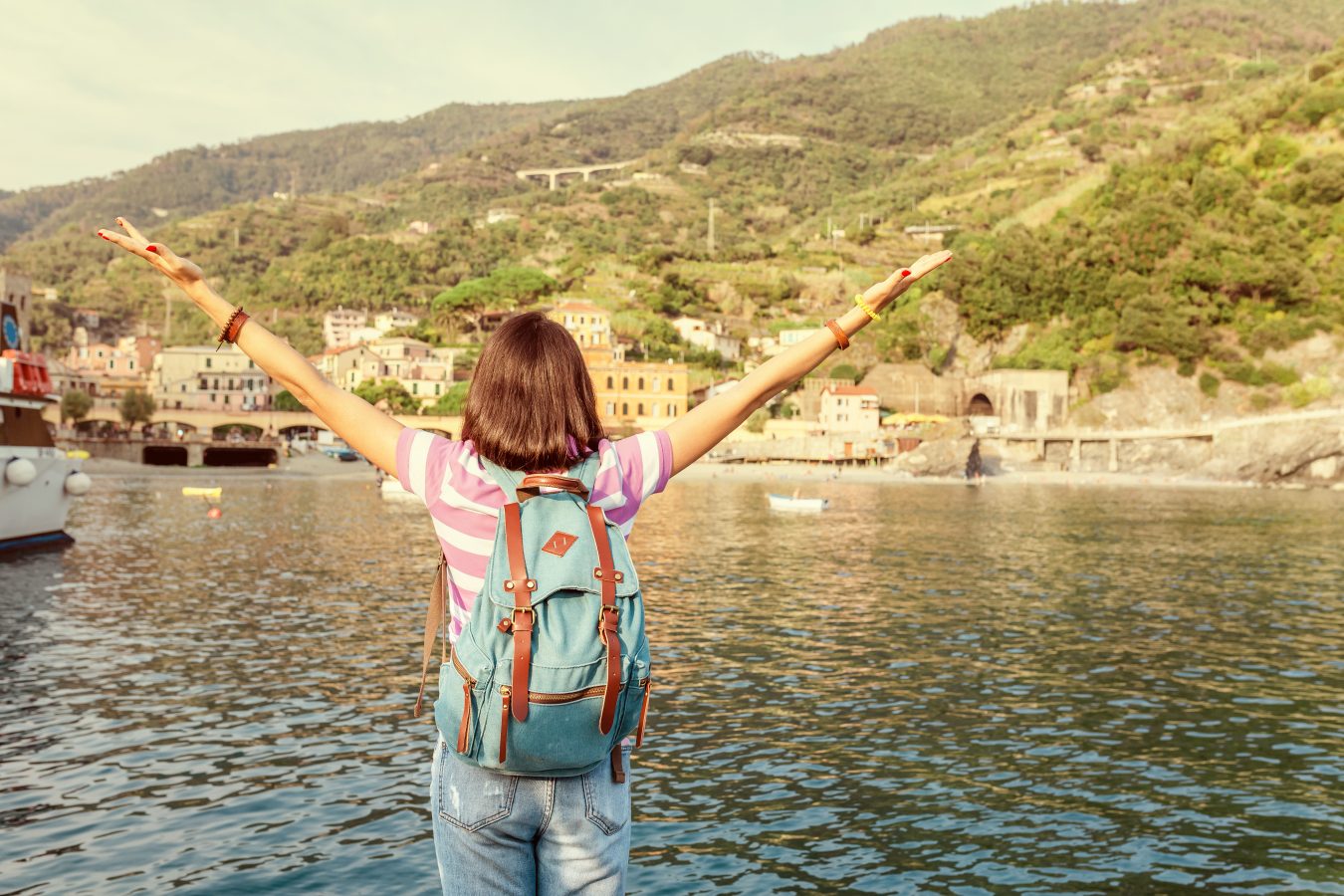 Young woman traveling in Italy takes in the seascape and town in the cliffs beyond it while their for cultural immersion.