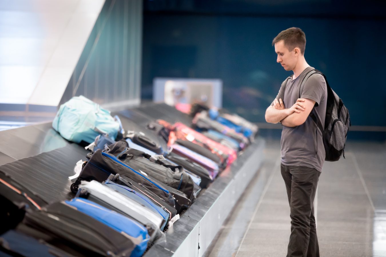 Passenger with carry-on backpack waiting at conveyor belt to pick his luggage in arrivals of airport terminal.