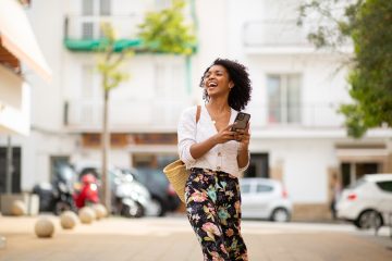 Portrait happy young african american woman with cellphone in city