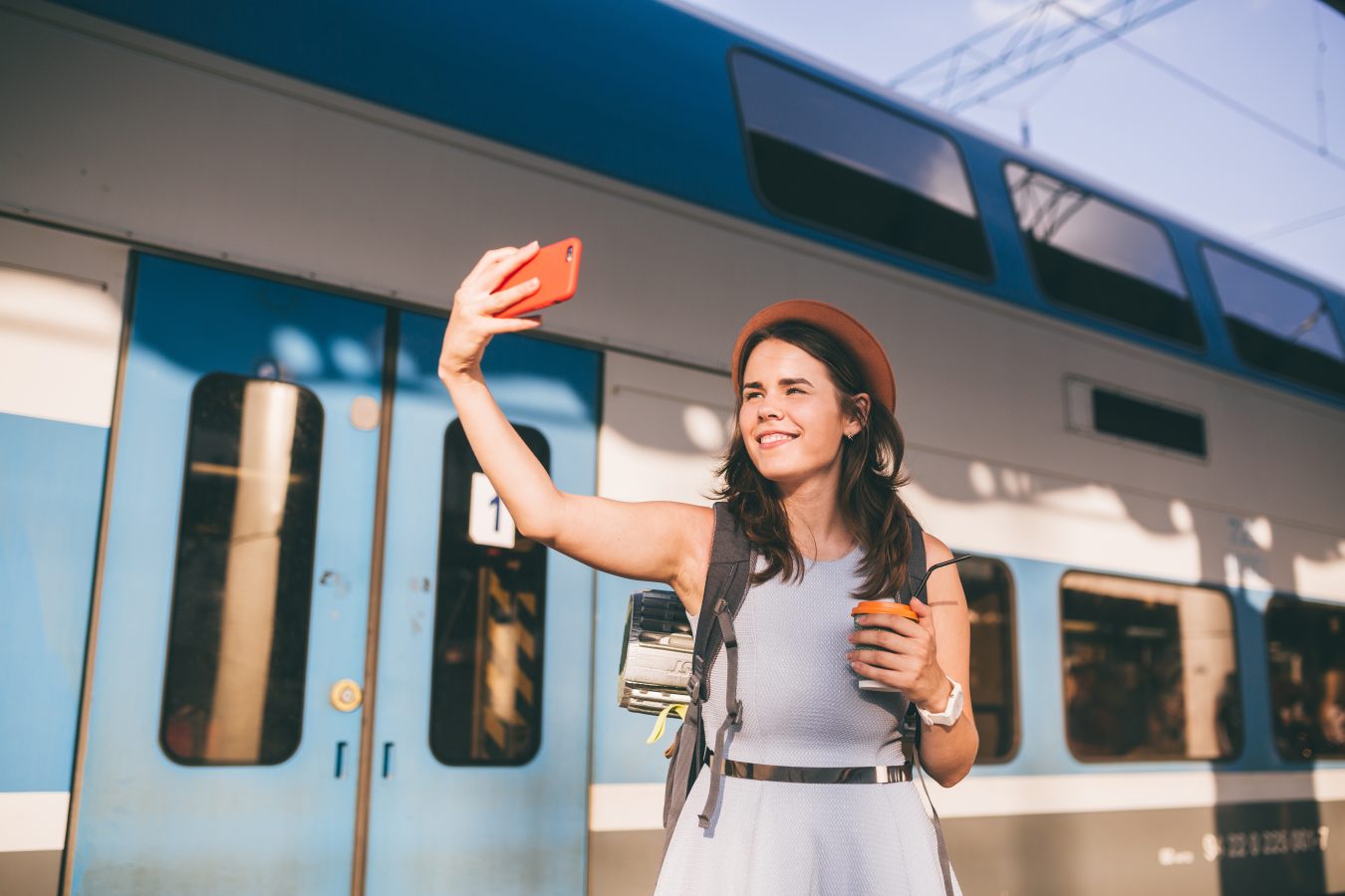 Young solo student traveler takes a selfie with her coffee while at the train station.