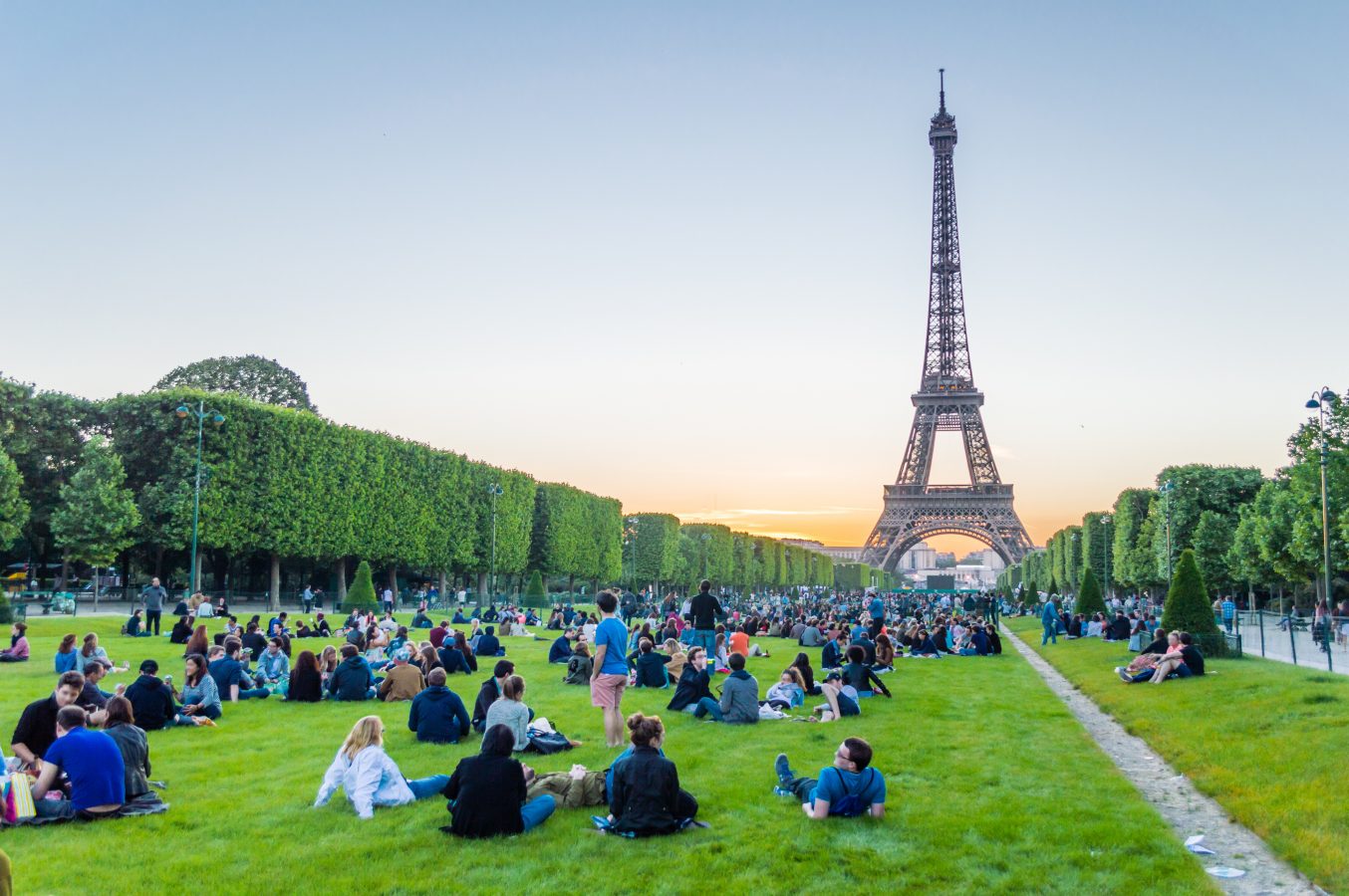 Eiffel Tower and people sitting on the grass watching sunset in Paris, France - one of the great things to do in Europe that isn't expensive.