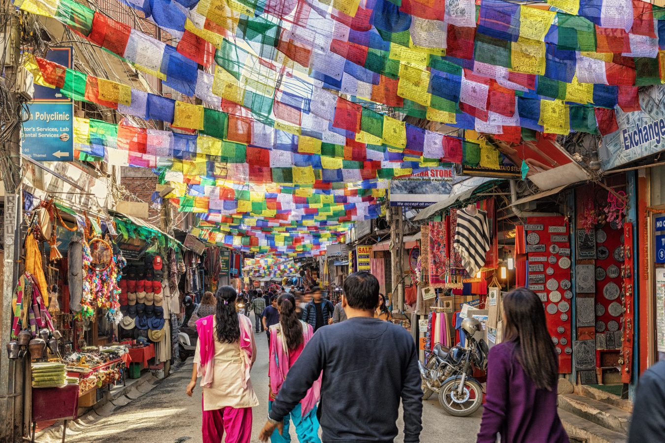 Individuals walking a street in Kathmandu, Nepal with Tibetan prayer flags hanging above heads. Nepal is one of the best places to visit in Asia.