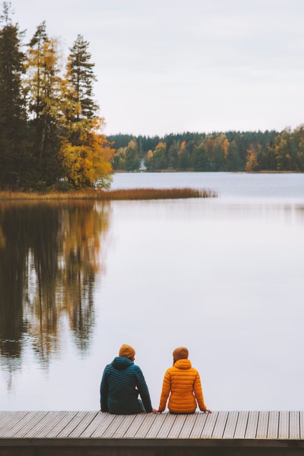 Two people sit by lakeside in autumn with leaves changing.