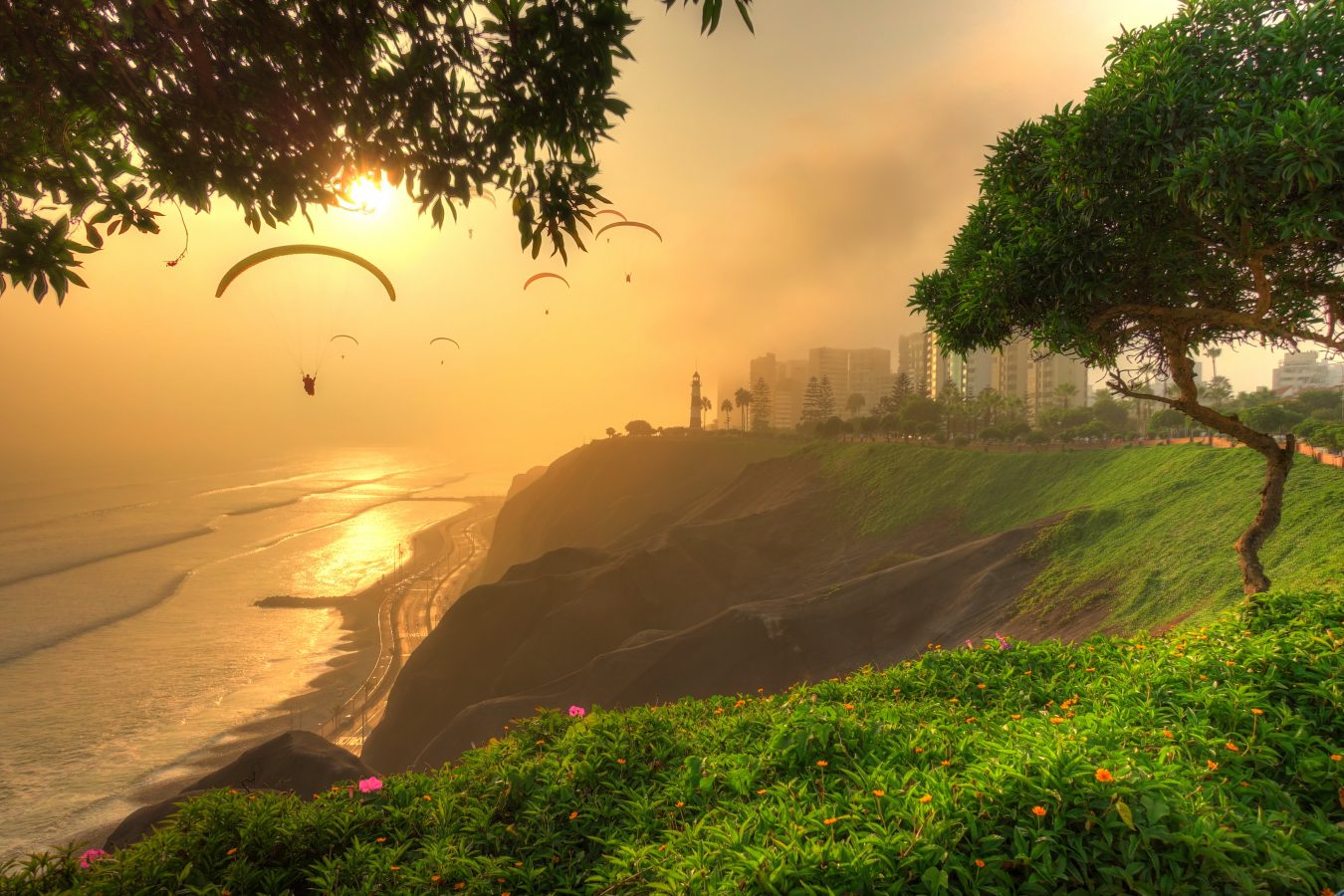 Miraflores district in Lima, Peru with the city in the right and then a steep cliff dropping out to a beach and paragliders floating in the sunset sky