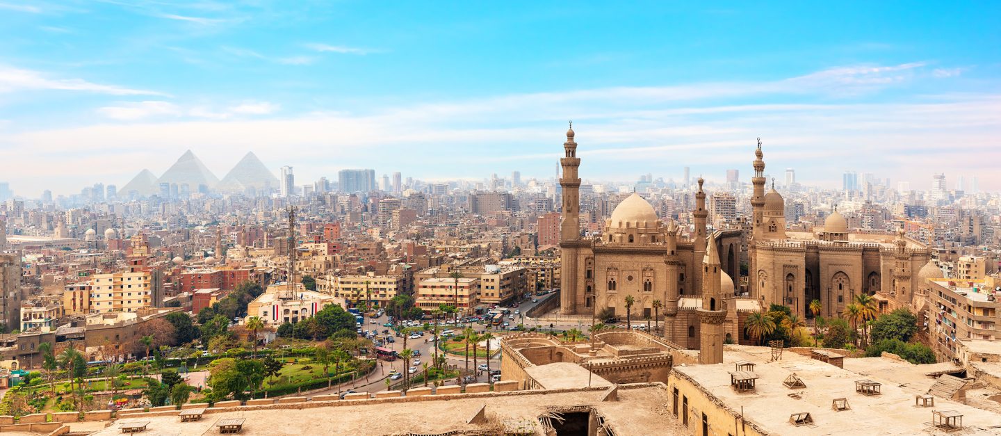 The Mosque-Madrassa of Sultan Hassan in the panorama of Cairo, Egypt with the pyramids in the distance.