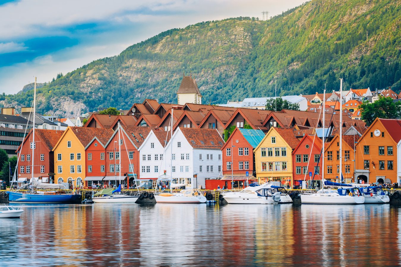 The coastline of Bryggen in Bergen, Norway with colorful scandinavian buildings along the water and a mountain in the background. Norway is a great trip in to take in 2025.